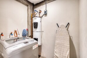 Une buanderie équipée d’un lave-linge, d’un chauffe-eau et d’une planche à repasser escamotable.
