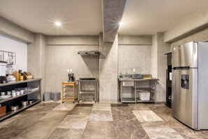 Een moderne keuken met een roestvrijstalen koelkast, een koffieapparaat en een magnetron. Er staan twee afvalbakken en een klein houten karretje.