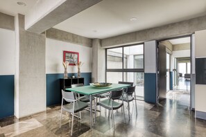 Een moderne eetruimte met een glazen tafel, metalen stoelen en een wand van beton.