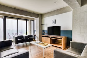 Ein modernes Wohnzimmer mit Flachbildfernseher, Ledersofas, einem Couchtisch und einem großen Fenster.