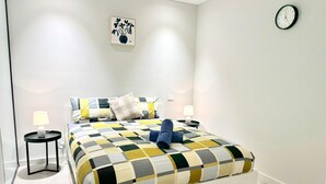 Quarto moderno com uma cama grande, duas mesas de cabeceira, um relógio de parede e uma obra de arte emoldurada acima da cama.