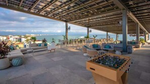 An outdoor seating area with a foosball table, lounge chairs, and a view of the sea. - Udara PH-I | 8th Floor 3BR Beachfront + Rooftop Pool, Spa, Sauna & Padel Court (Bucerías)