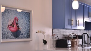 Une cuisine moderne avec des meubles bleus, un plan de travail blanc, un grille-pain et un luminaire suspendu.