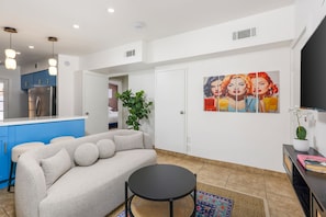 A modern living room with a beige sofa, a round black table, and a colorful rug.