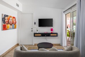 Una sala de estar moderna con un sofá, un televisor de pantalla plana, una mesita y un ventanal corredizo que da a un espacio exterior.