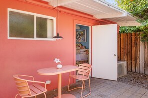Un pequeño patio con una mesa redonda y dos sillas, una puerta blanca y una valla de madera al fondo.
