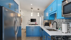 A modern kitchen with blue cabinets, a stainless steel refrigerator, a black stove, and a white countertop. - The Duo Suite 2 King Bedrooms Suite, Pool, Hot Tub (Palm Springs)
