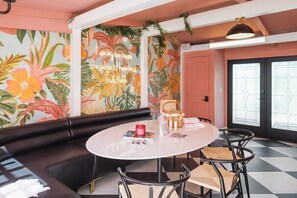 Une pièce comprenant un canapé en cuir noir, une table ronde avec des chaises, un mur décoratif orné de motifs floraux et une porte avec des panneaux en verre dépoli.