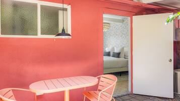 A room with a red wall, a white door, a bed with patterned bedding, and a small table with two chairs.