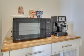 Una cocina con microondas, cafetera y tazas coloridas sobre la encimera.