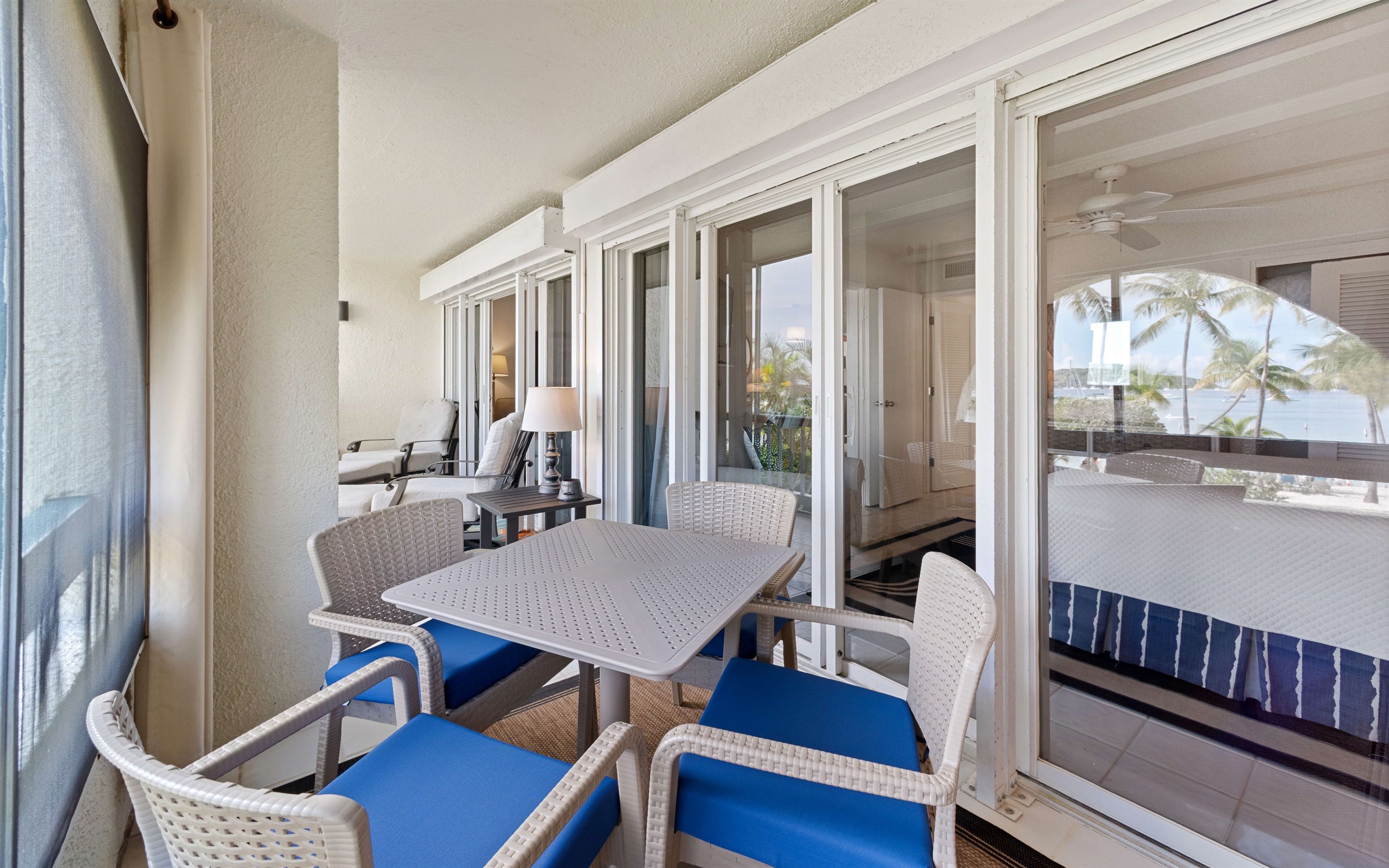 A balcony with wicker furniture and a table, overlooking a pool and palm trees.