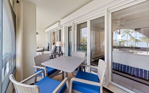 A balcony with wicker furniture and a table, overlooking a pool and palm trees. - On the Beach | Pool + Hot Tub + Restaurant | Gated (St. Thomas)