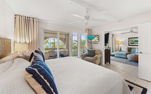 A hotel room with a large bed, a balcony with a view of the ocean, a seating area with a TV, and a ceiling fan. - On the Beach | Pool + Hot Tub + Restaurant | Gated (St. Thomas)