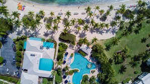 Vista aérea de un resort con una gran piscina, una playa y palmeras.