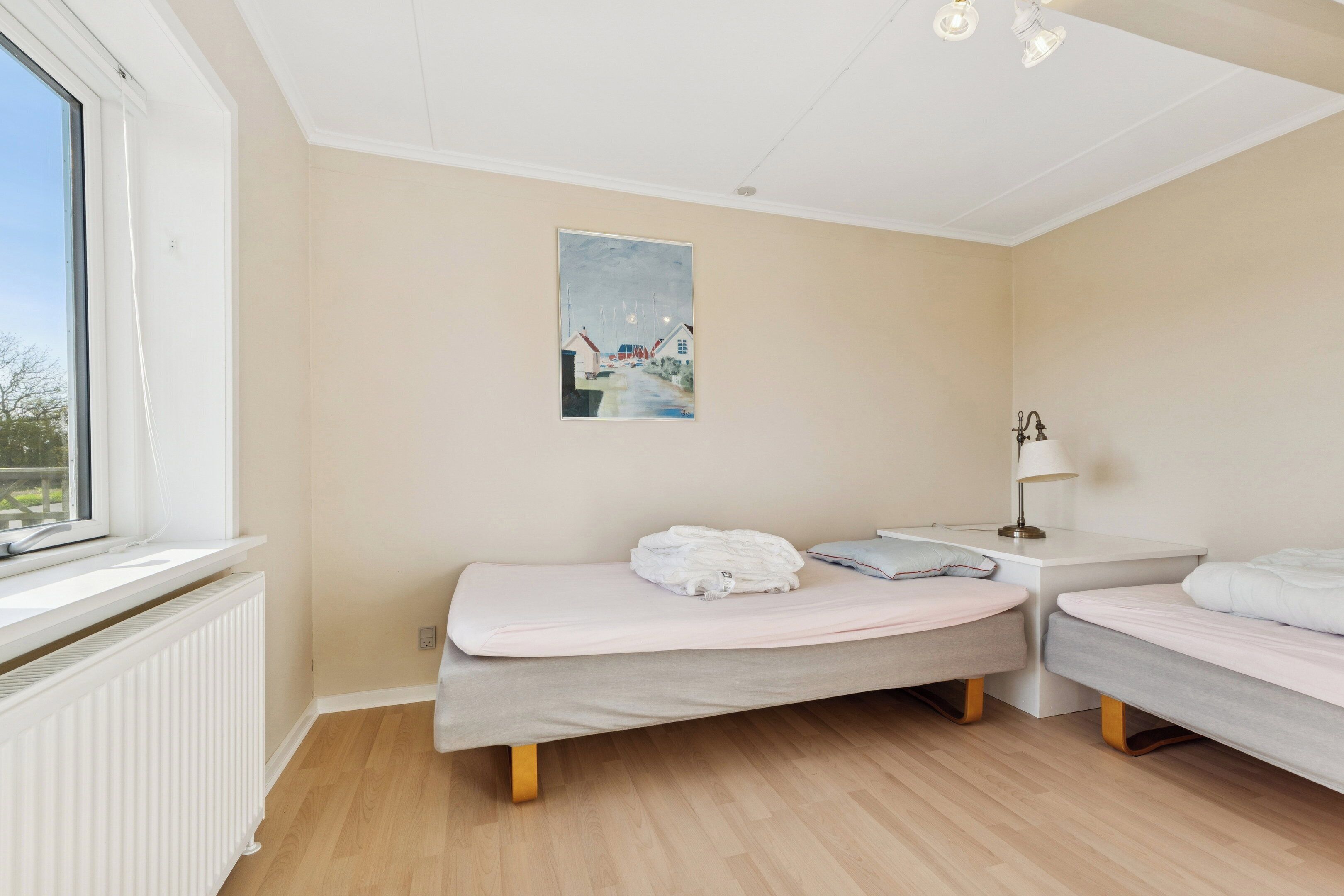A bedroom with two single beds, a window, a radiator, and a painting on the wall.