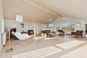 Un'ampia zona giorno con soffitto alto, pavimento in legno e grandi finestre.