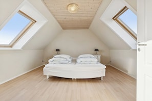 Una camera da letto con soffitto spiovente, lucernari, un letto con cuscini, comodini e pavimento in legno.