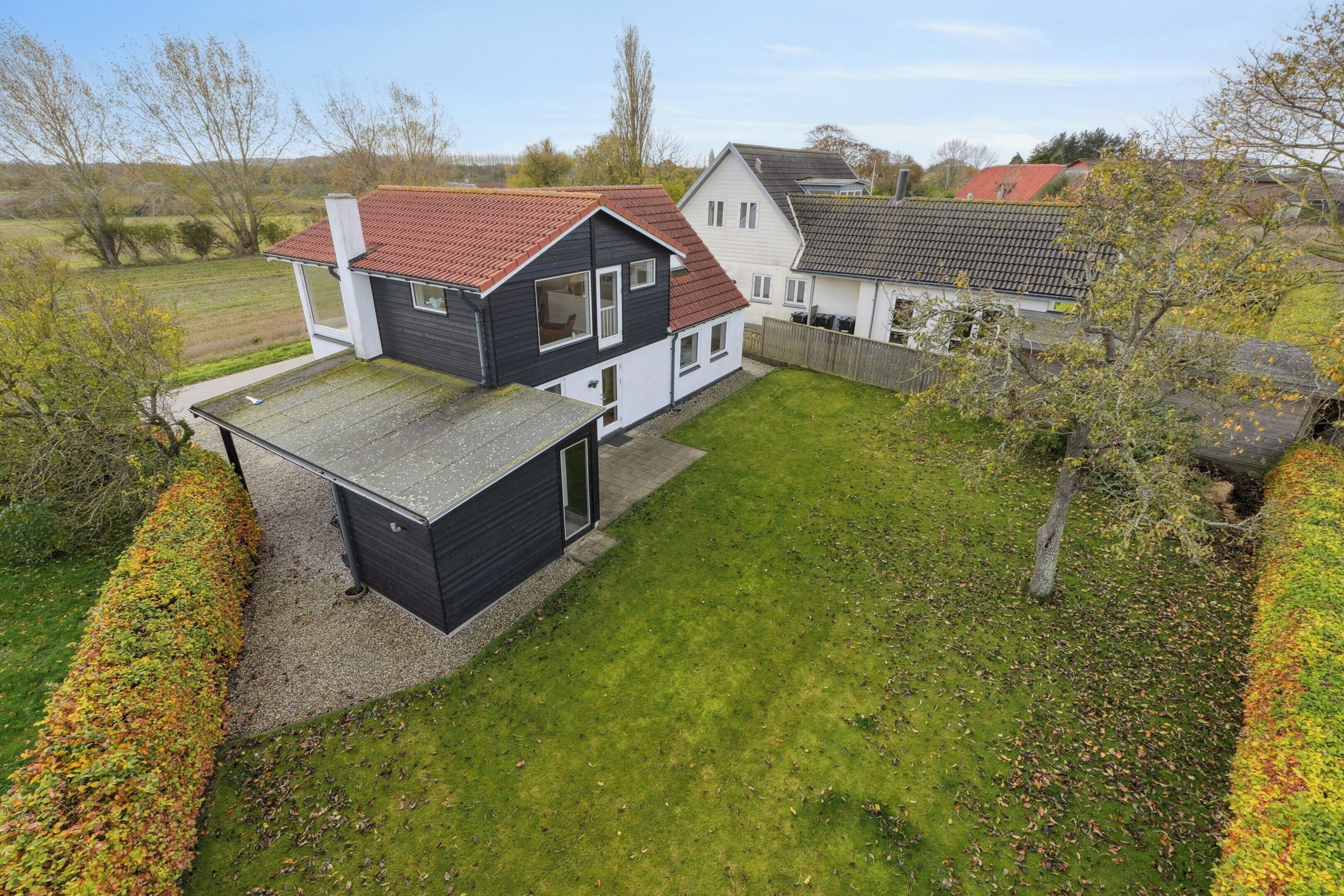 Une maison moderne à deux étages, avec un toit recouvert de tuiles rouges, un petit garage attenant et une pelouse bien entretenue.