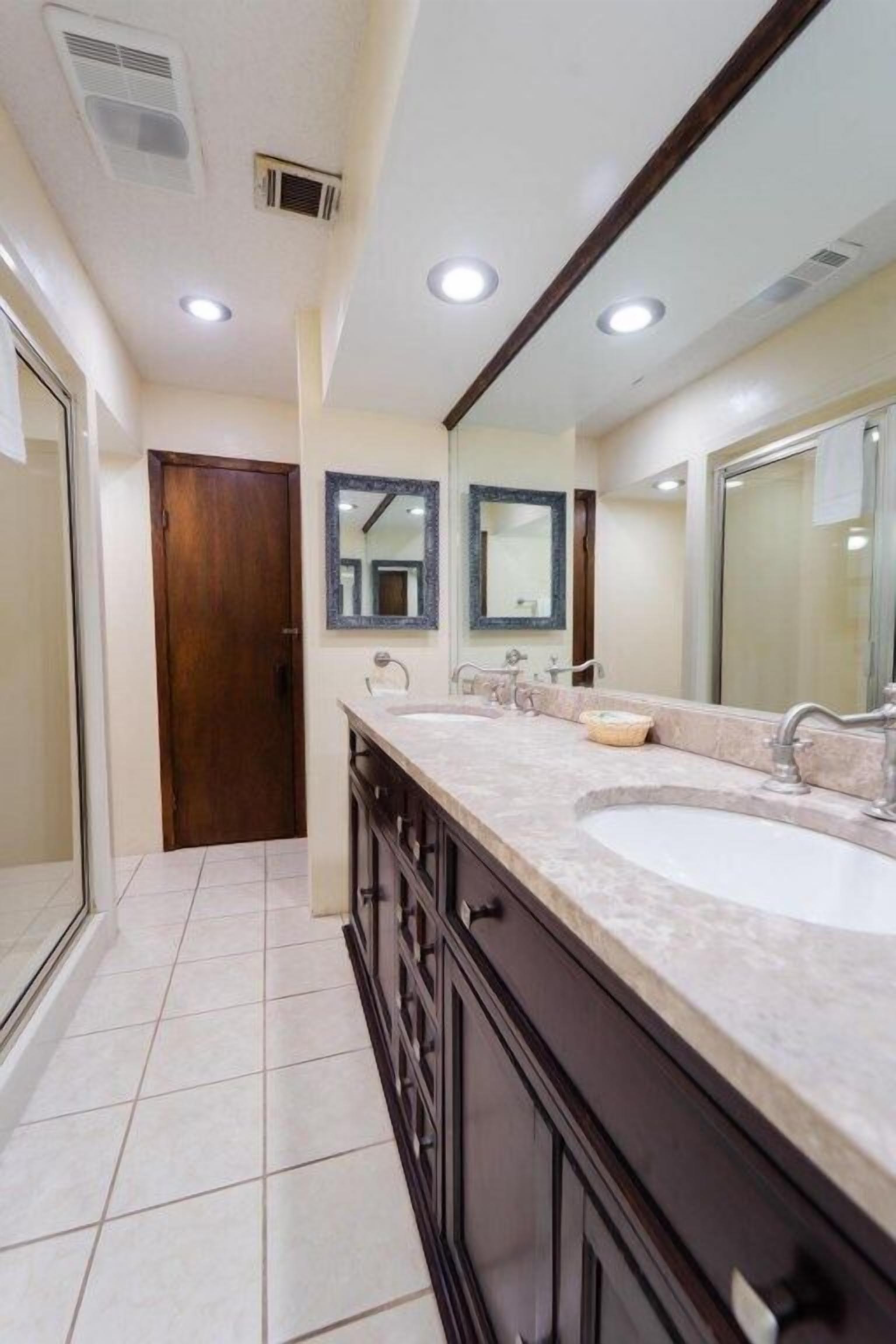 Une salle de bain moderne avec un meuble-lavabo à deux vasques, un grand miroir et des spots encastrés au plafond.