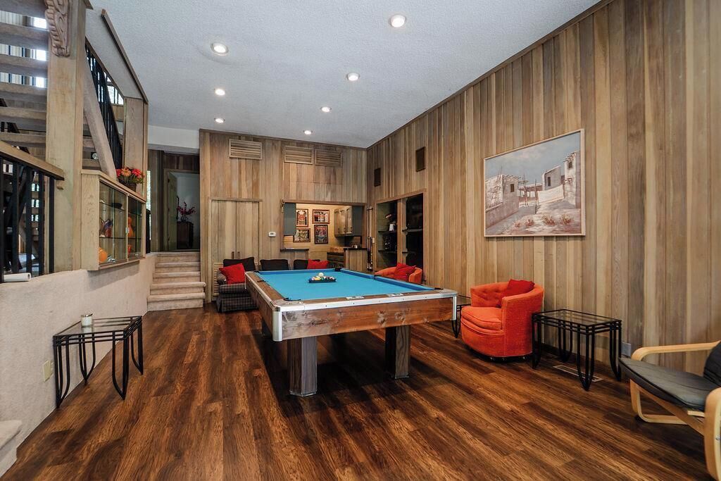 A spacious room with a pool table, comfortable seating, and a staircase leading to an upper level.