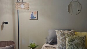 Un dormitorio con cama, una lámpara de pie, una planta pequeña y un espejo montado en la pared.