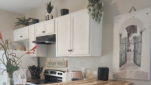 Una cocina con armarios blancos, encimera de madera, estufa y taburetes negros.