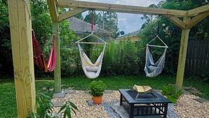 Una pérgola de madera con dos hamacas colgantes, una mesa y plantas en macetas en un patio trasero.