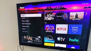 Televisor de pantalla plana montado en la pared que muestra una interfaz de Roku con diversos servicios de transmisión.