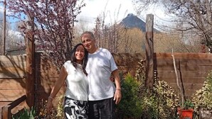 A couple standing in a garden with a wooden fence, potted plants, and a chicken. - Los Colibríes duplex for rent (pet friendly) (Chubut)