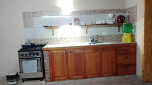 A kitchen with a stove, oven, wooden cabinets, a sink, and a green water dispenser. - Los Colibríes duplex for rent (pet friendly) (Chubut)