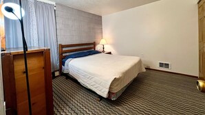 Una habitación de hotel con cama, escritorio, lámpara y armario.