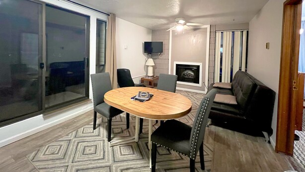 Una sala moderna con una mesa redonda de madera, dos sillas negras, un sofá negro, un televisor montado en la pared y una chimenea.