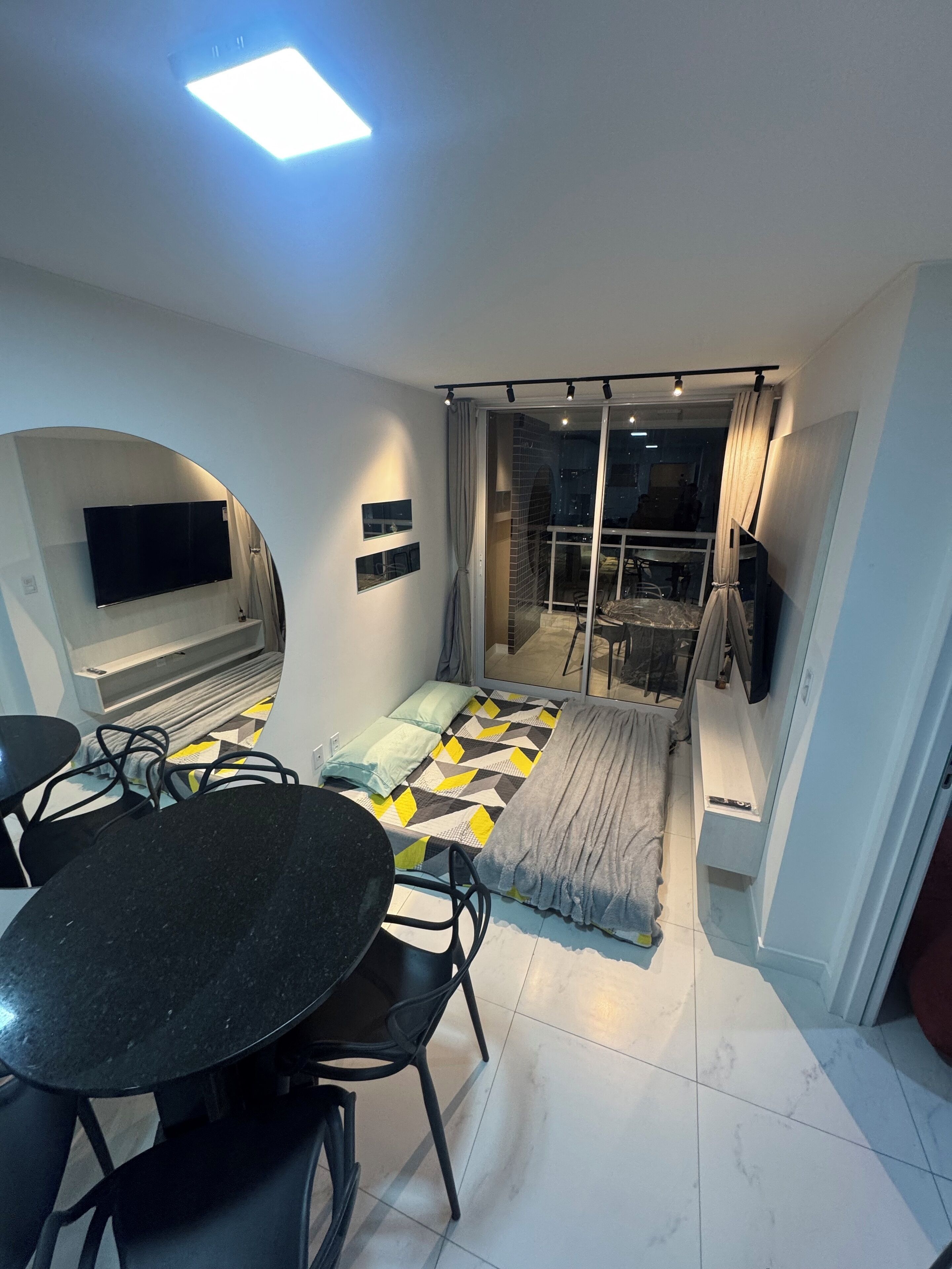 A modern living room with a black dining table, a sofa, and a TV mounted on the wall.