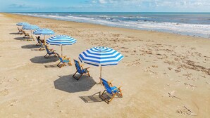 Une plage bordée de rangées de parasols bleus et blancs et de chaises longues assorties.