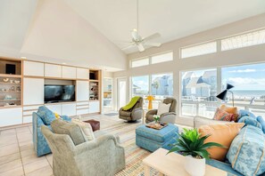 A spacious living room with a large TV, comfortable seating, and a balcony with a view. - Too Much Fun - Retro Chic, Cool Beach Retreat (Galveston)
