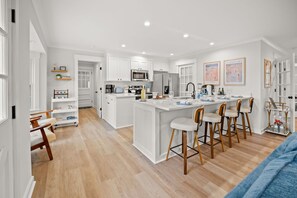 A modern kitchen with white cabinetry, a central island with bar stools, and a dining area with a blue sofa. - Hidden Gem • Close to Downtown & Beaches, 8 Guests (Charleston)