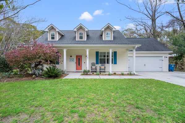 A two-story house with a front porch, a red door, and a garage.