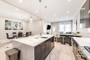 Een moderne keuken met een groot eiland, inbouwapparatuur en een eethoek met een tafel en stoelen.