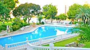 Piscina amb tanca blanca, envoltada de vegetació i arbres.