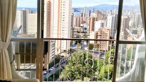 Habitació amb una finestra gran que ofereix vistes a la ciutat, un sofà amb un coixí i una làmpada al sostre.