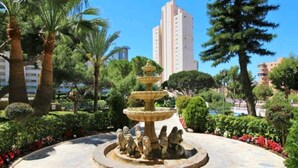 Una font rodona amb diversos nivells, envoltada d'un jardí ben cuidat amb diferents plantes i arbres.