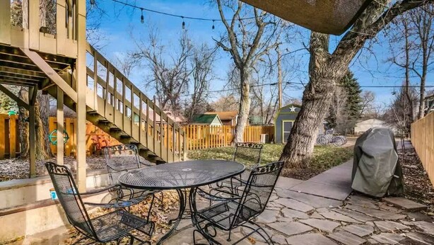 An outdoor patio with a stone table and metal chairs, surrounded by trees and a wooden fence. - Old Town Putting Green - King bed comfort (Fort Collins)