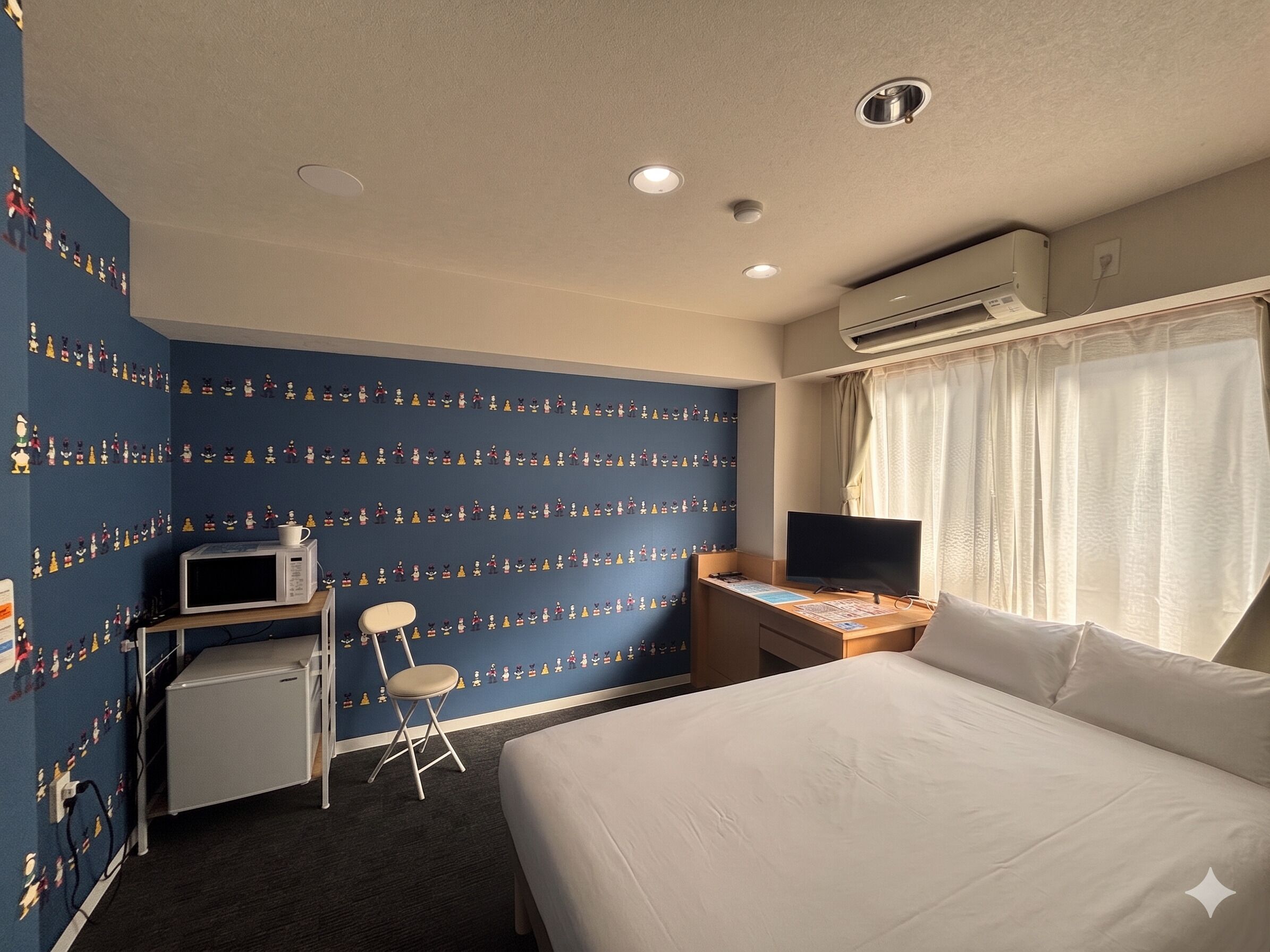 A hotel room with a bed, desk, chair, microwave, and air conditioning unit.