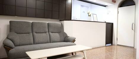 A room with a grey sofa, a small white table, and a dark cabinet.