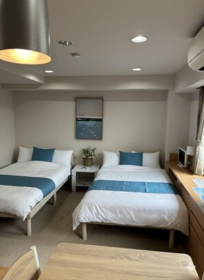 A hotel room with two beds, a small table, a chair, a desk with a computer, and a wall-mounted TV. - Hotel Leap (Osaka)