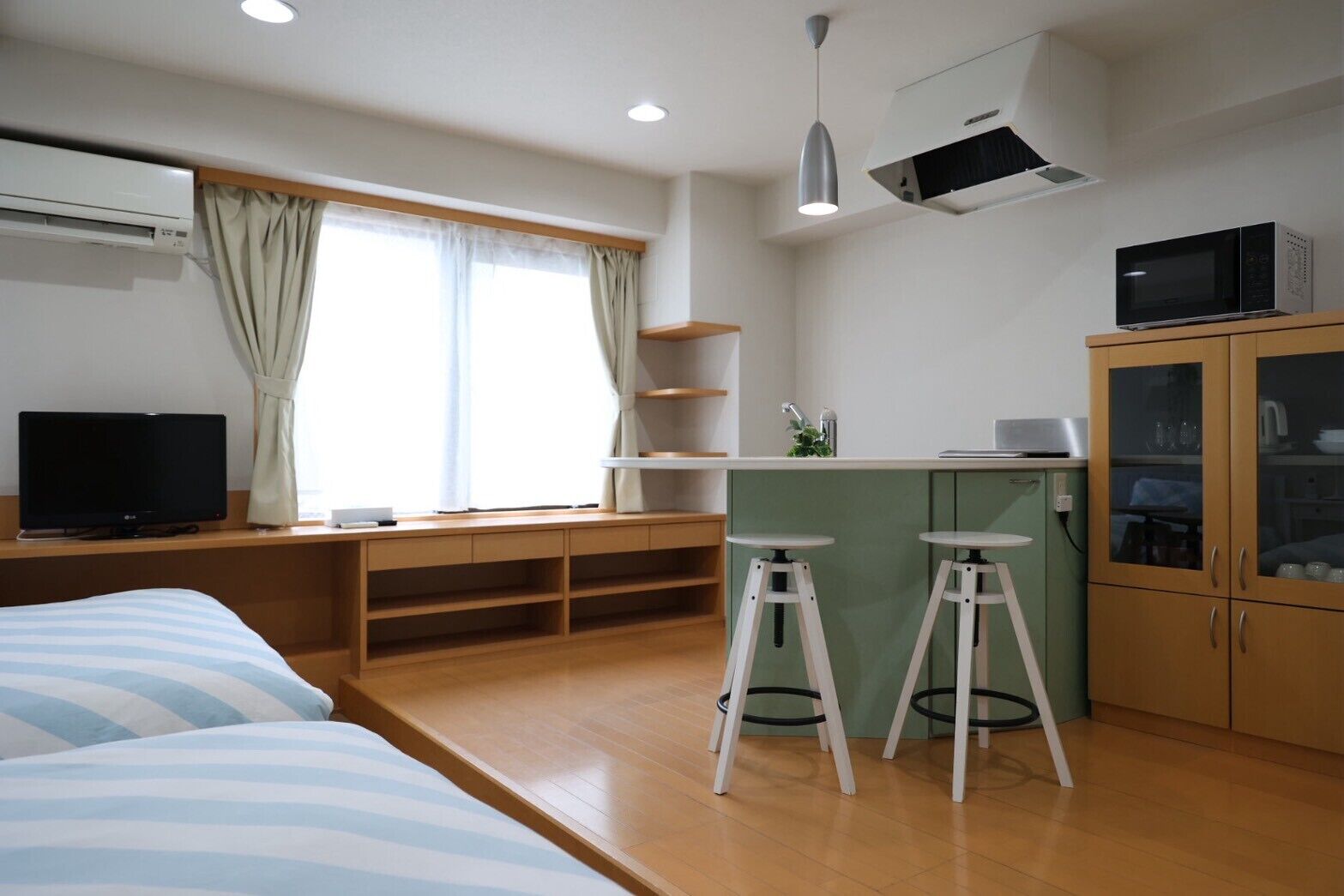Een kleine hotelkamer met een bed, een televisie, een kitchenette en een raam met gordijnen.