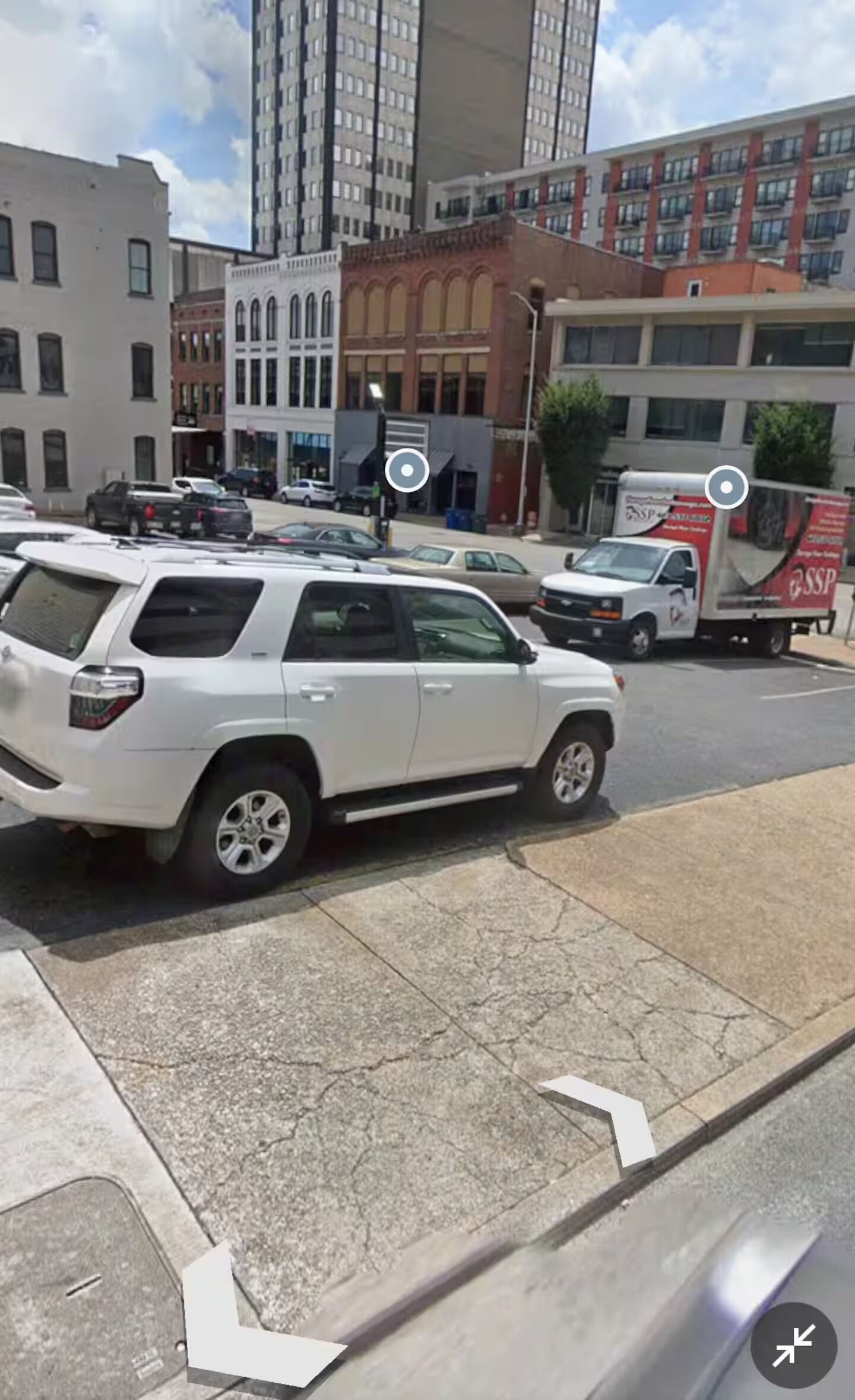 A white SUV parked on a city street with buildings in the background.