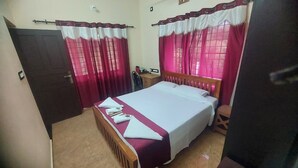 A bedroom with a bed, curtains, a bedside table, and a chair. - Blue Hills View - Serviced Villa in Attapadi,Kerala -rooms with mountain view (Attapadi, Palakkad)