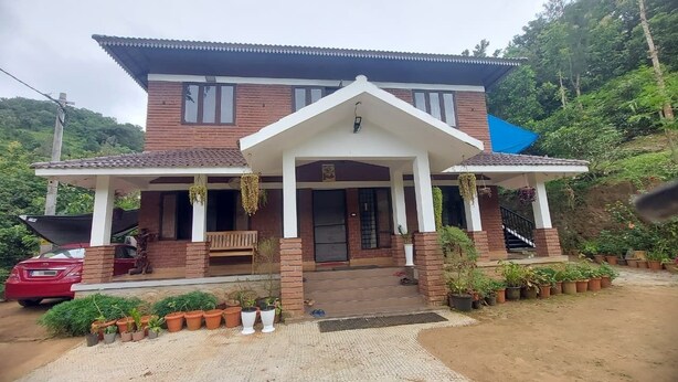 A two-story house with a porch, potted plants, and a red car parked in front. - Blue Hills View - Serviced Villa in Attapadi,Kerala -rooms with mountain view (Attapadi, Palakkad)
