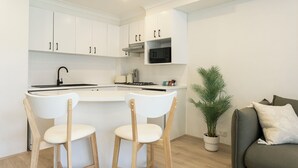 Cozinha moderna com armários brancos, uma ilha central com dois bancos altos, um micro-ondas e um vaso de planta.